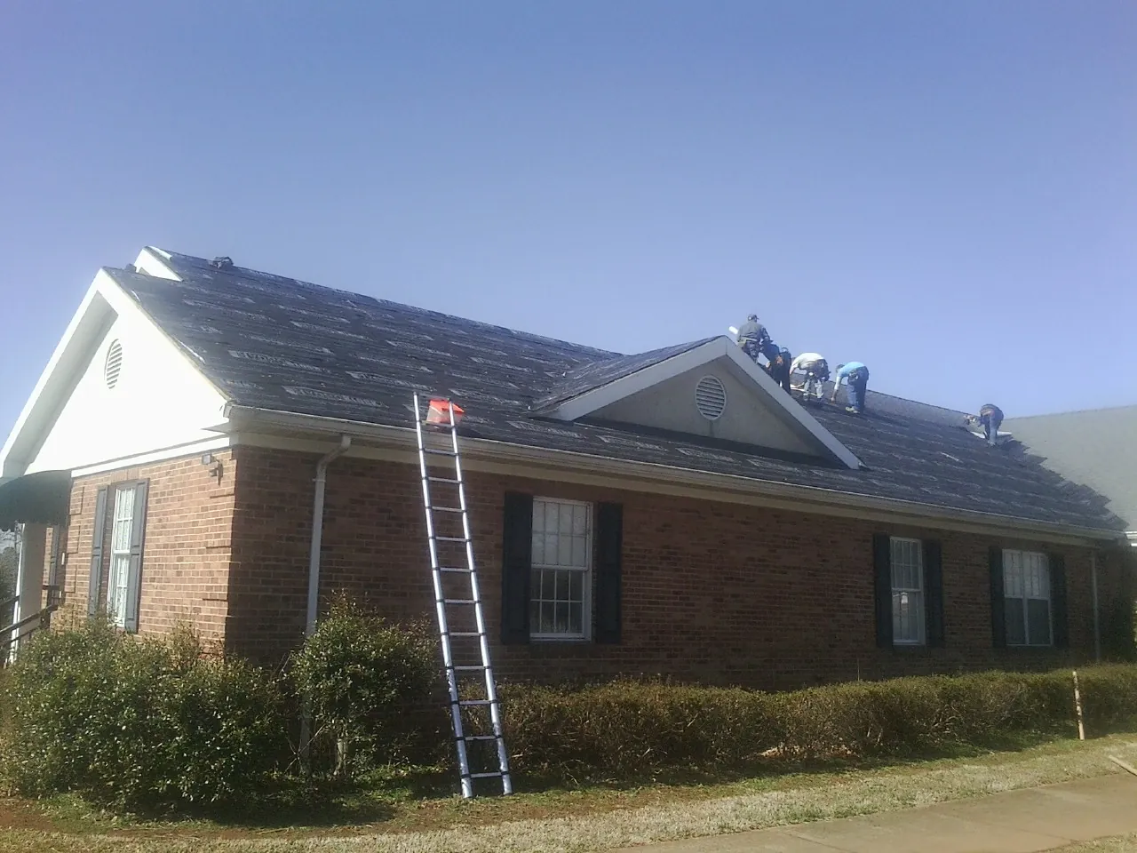 Crew tearing shingles off a brick ranch roof with a ladder set — Emergency Roof Repair work by our crew in Liberty Hill