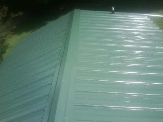 New green metal panels meeting at the ridge of a roof — Flat Roof Repair work by our crew in Liberty Hill