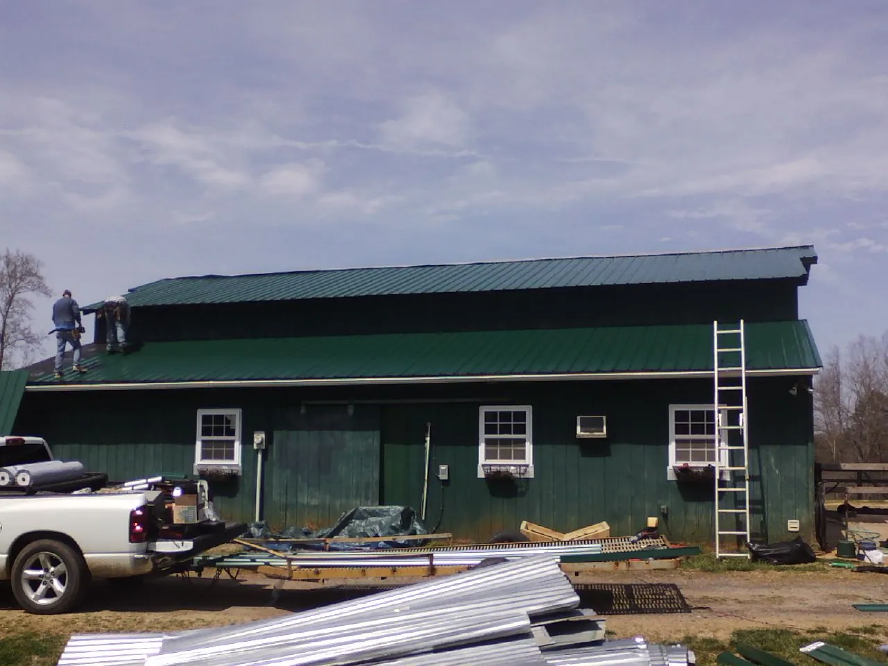 Crew installing green metal roofing on a large green barn in Liberty Hill