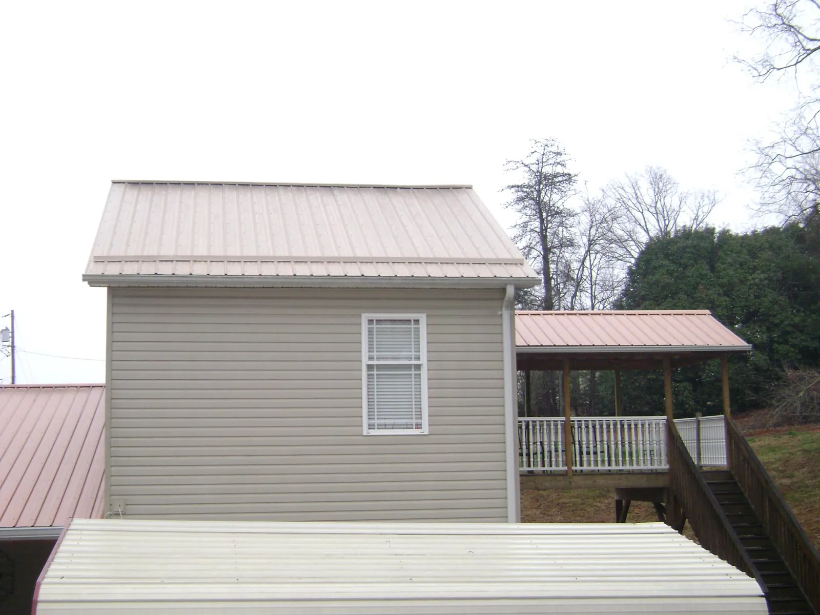 Tan metal roofs on a two story addition and attached porch, from a Roof Replacement job in Liberty Hill